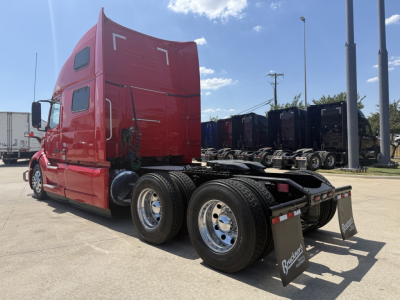 Volvo VNL64T860 truck chassis and sleeper cab side view showing rear wheels and fifth wheel, red cab, black chassis, dealership lot.