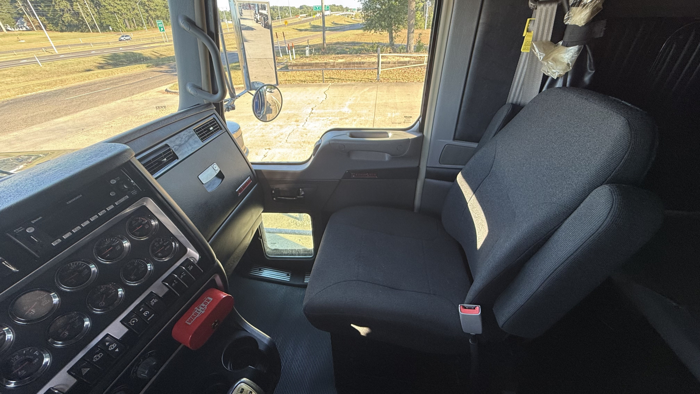 Kenworth W900 interior cab view showing steering wheel, dashboard gauges, and driver seat in a sleeper truck.
