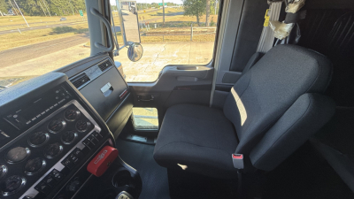 Kenworth W900 interior cab view showing steering wheel, dashboard gauges, and driver seat in a sleeper truck.