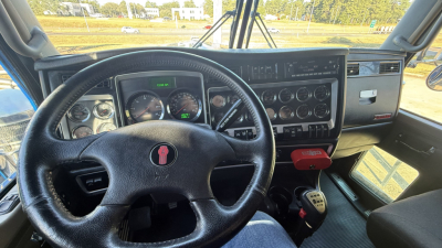 Kenworth W900 interior dashboard and steering wheel with gauges and controls visible, PRND shifter, pedal area, and windshield.