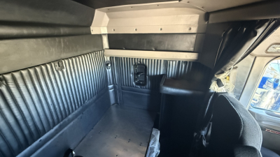 Kenworth W900 truck interior view of sleeper area showing corrugated metal side panels and cabin roof, with a small storage area and seatback in the foreground.