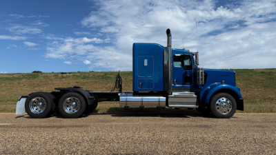 Conventional sleeper Kenworth W900 truck profile in blue, side view showing cab, exhaust stack, and dual rear axles.