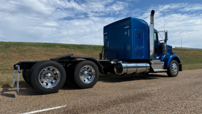 Kenworth W900 truck cab and chassis in blue, side view showing sleeper cab, dual rear axles, chrome fuel tanks, and exhaust stack.