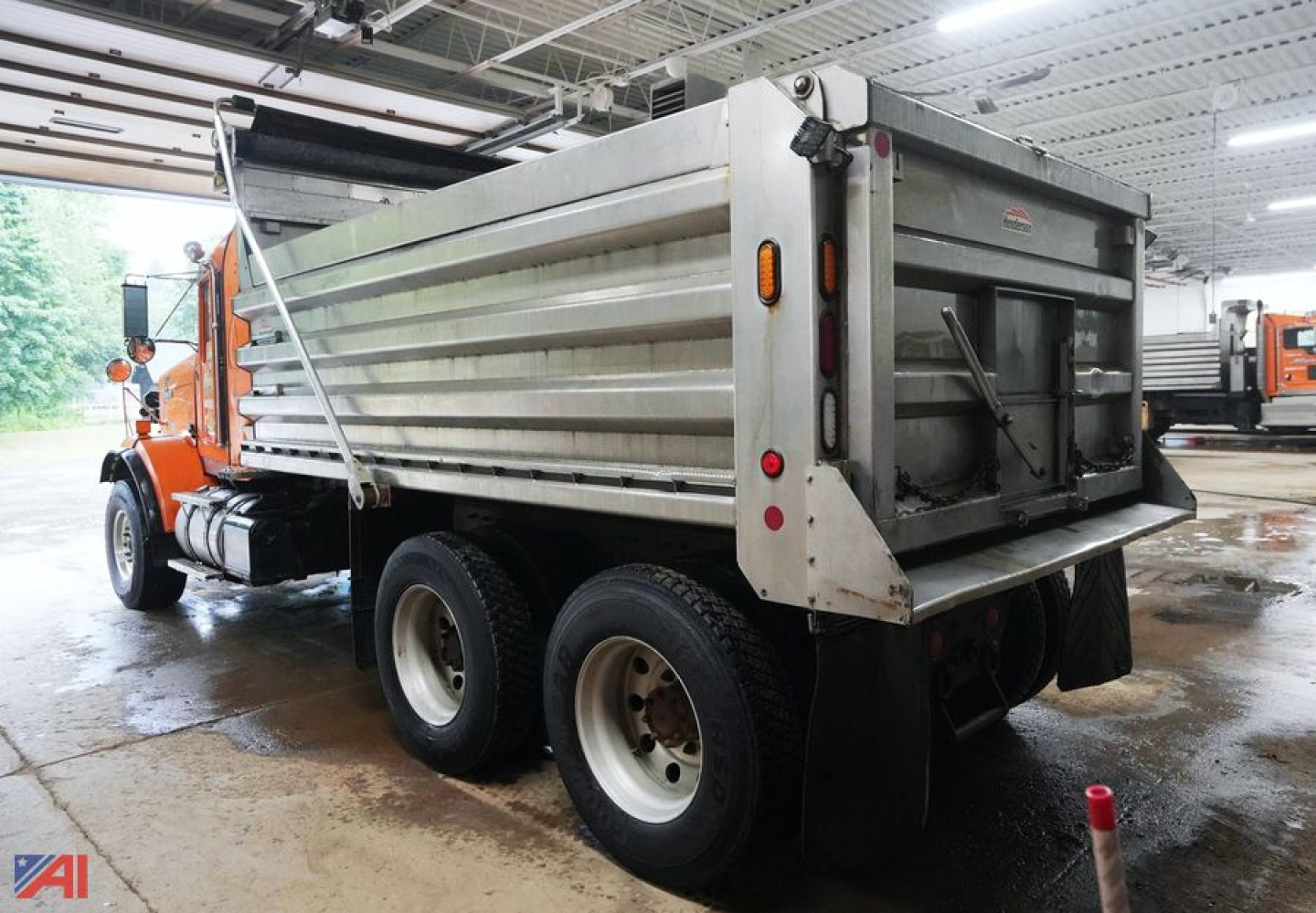 Kenworth T800 dump truck with plow, side view showing dump hopper and rear tailgate under showroom lighting.