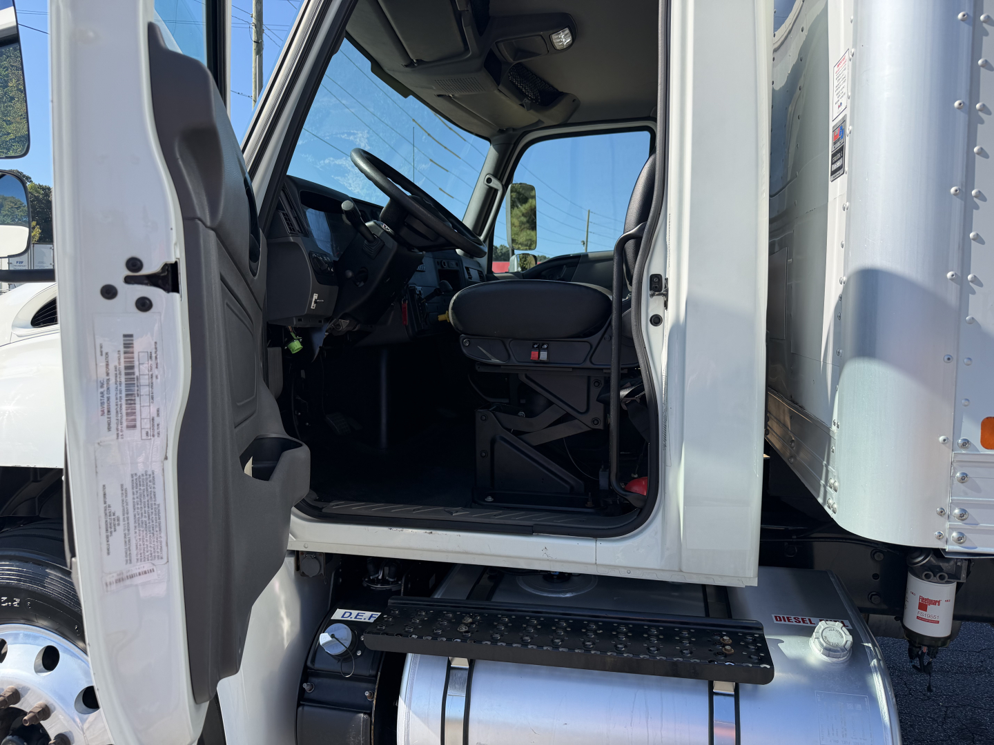 Truck cab interior of a 2022 International MV607 with open driver door, showing steps, steering wheel, and seat. Side of cab and entry step visible.