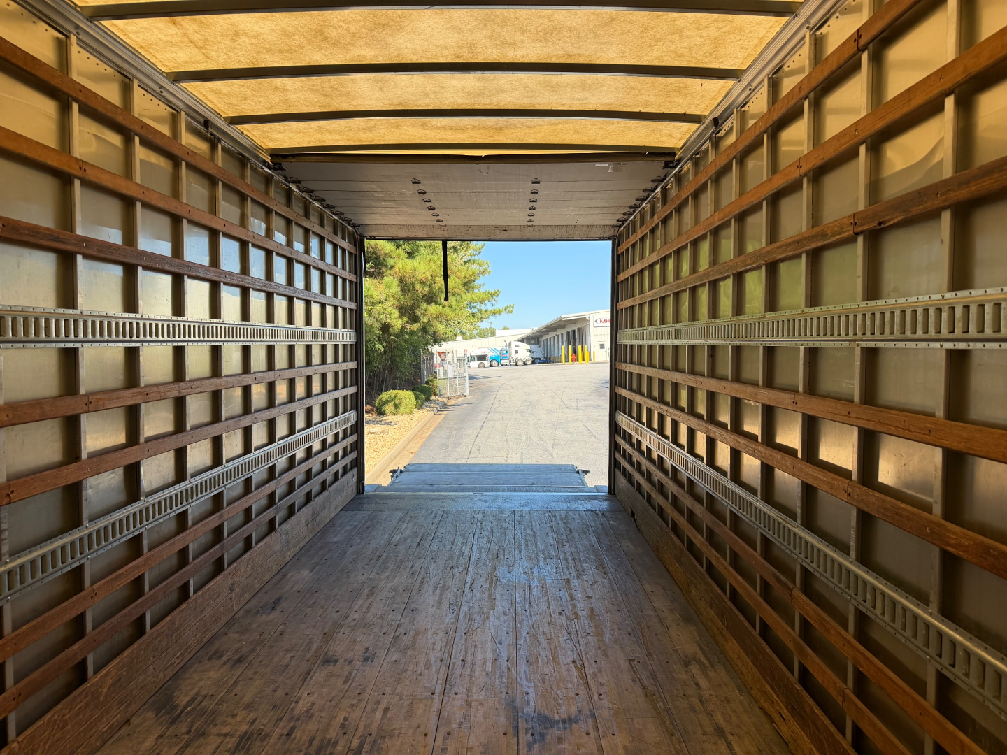 Truck trailer interior view looking forward through cargo area with metal side rails and wooden floor planks.