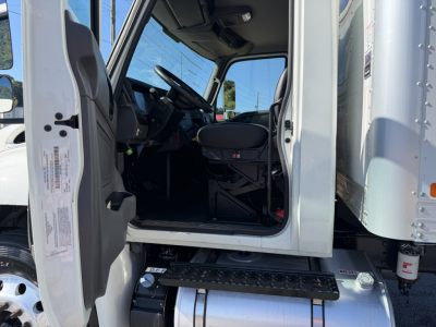Truck cab interior of a 2022 International MV607 with open driver door, showing steps, steering wheel, and seat. Side of cab and entry step visible.