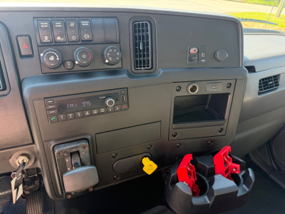 Dashboard of a 2022 International MV607 showing HVAC controls, radio, ignition, and cup holder area with yellow key tag and red battery disconnect handles.