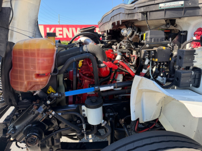 Truck engine bay showing coolant reservoir, various hoses, wiring, and engine components in a MV607 truck.