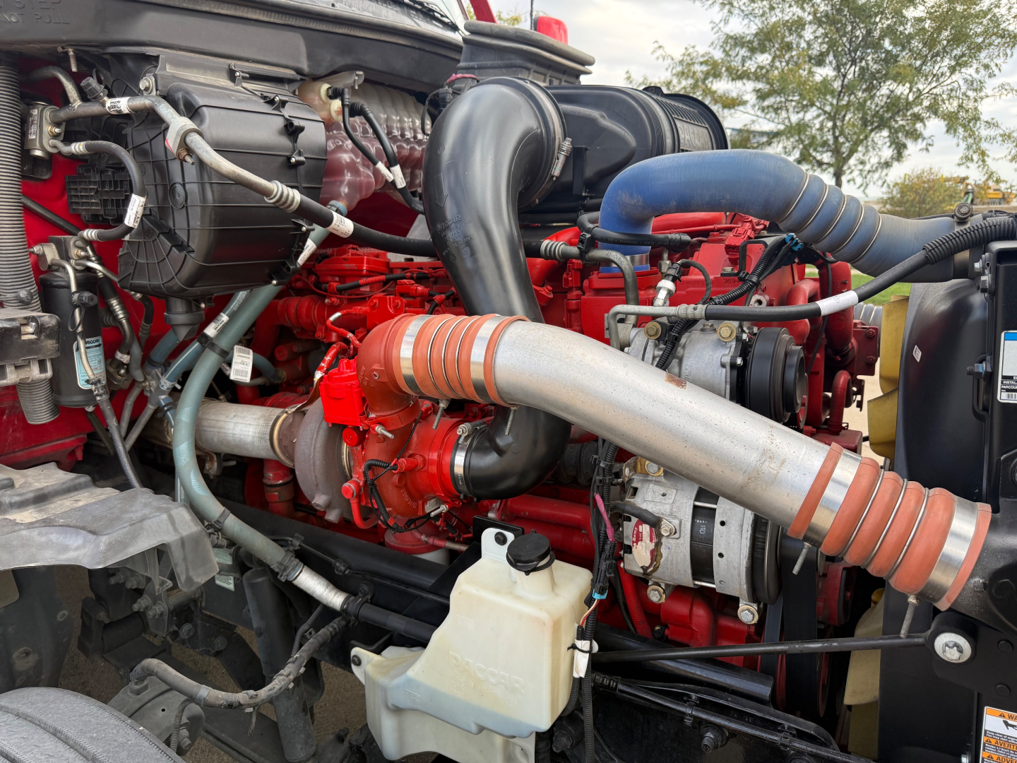 Kenworth T680 engine bay showing red engine block with turbocharger piping, hoses, and coolant reservoir