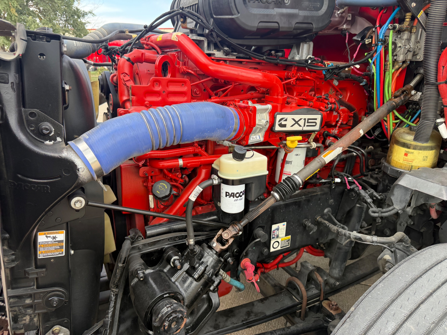 Kenworth T680 engine bay showing red X12 engine with blue air intake hose and PACCAR fluid reservoir label.