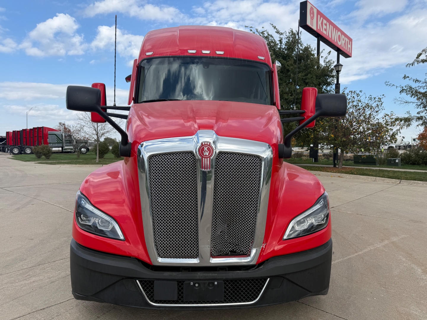 Kenworth T680 front view showing bold chrome grille with Kenworth emblem, red hood and bumper, black lower fascia, and side mirrors.
