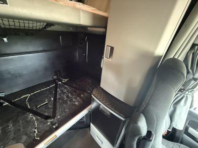 Kenworth T680 cab interior showing bunk area and storage cabinet with black floor, wires under bed, driver seat; no visible labels.