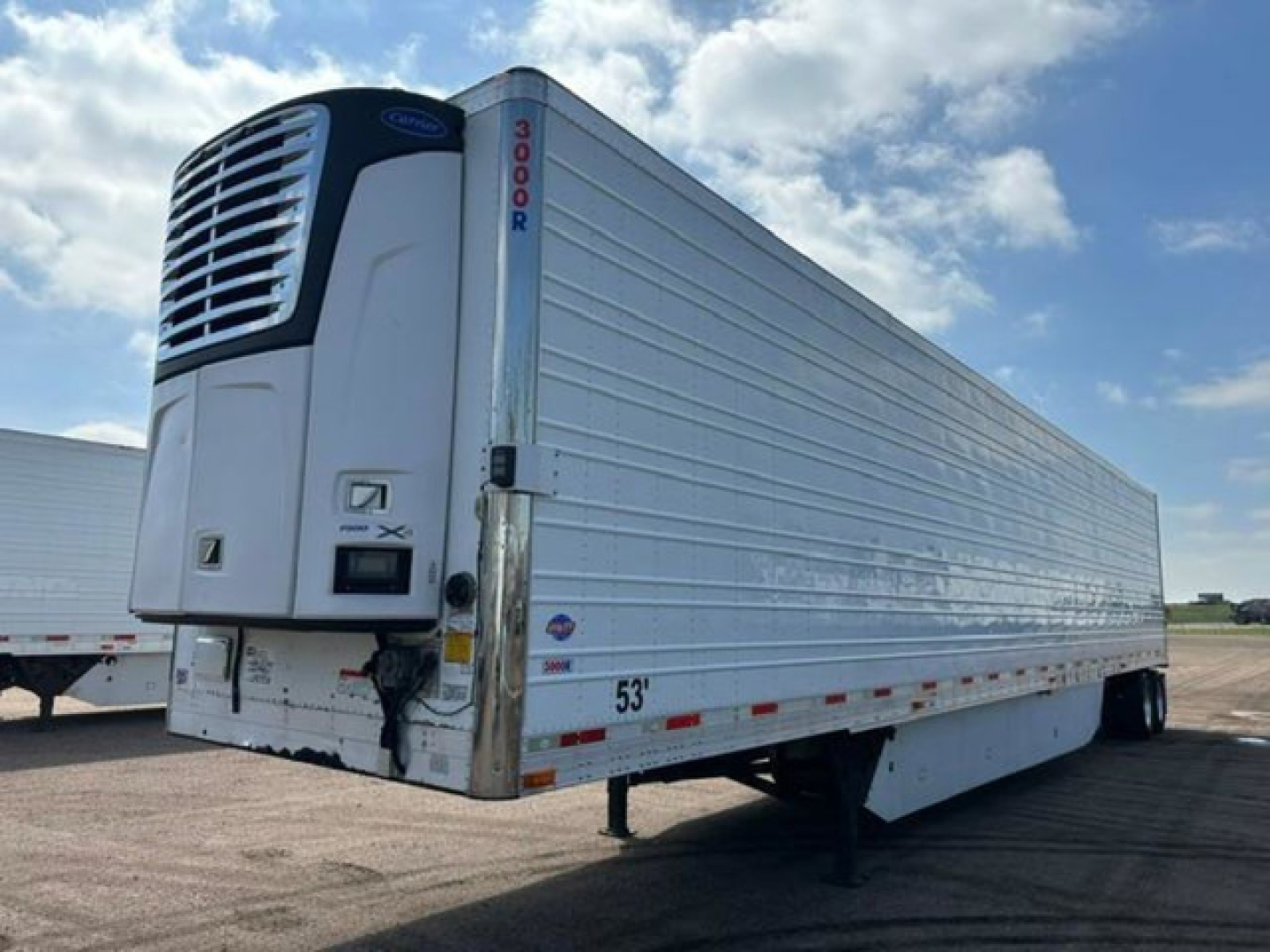 Front-left view of a 53-foot refrigerated trailer with a large Carrier reefer unit, white aluminum panels, and landing gear visible.