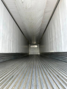 Interior view of a refrigerated trailer cargo area showcasing ribbed floor and side walls, long rectangular tunnel leading to rear, no visible labels.