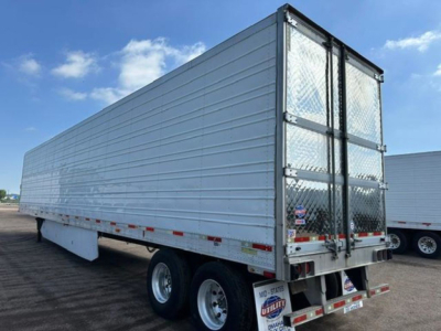 Utility reefer trailer side view showing aluminum siding, rear double doors, tandem axles, and DOT reflective tape.