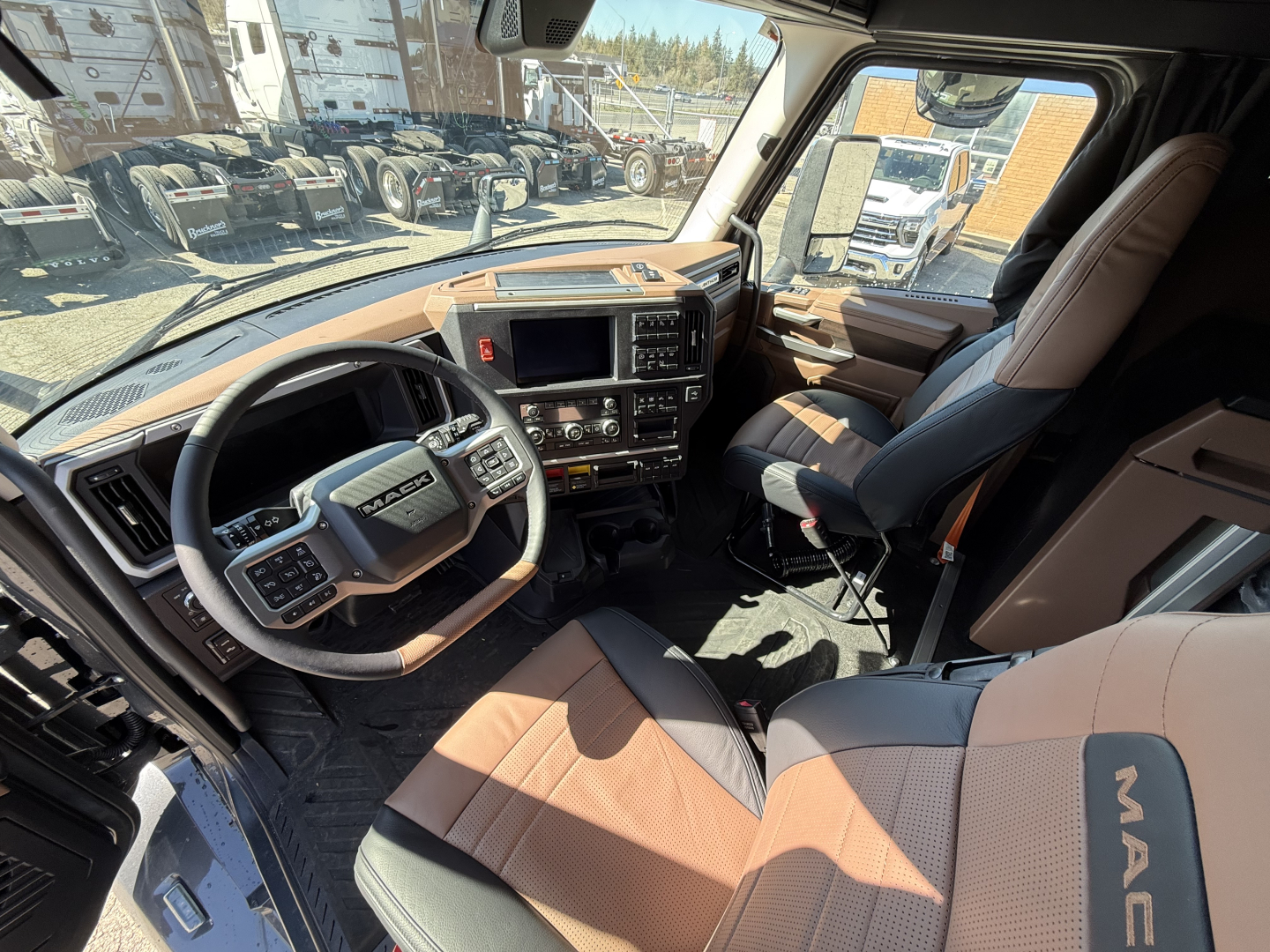 Interior of a 2027 Mack AN64T64 truck cab showing steering wheel, dashboard, center console, and tan/black seats.