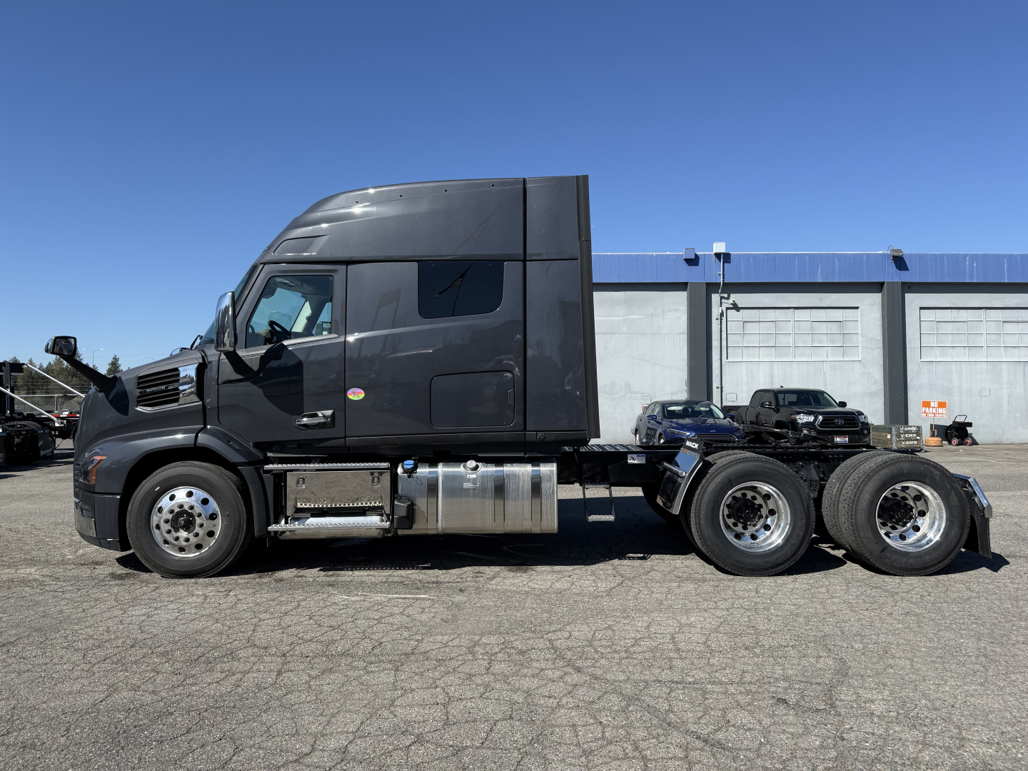 Truck side view showing a black Mack AN64T64 conventional sleeper tractor, with dual rear axles and fuel tanks visible, no visible text legible on the tractor surfaces.