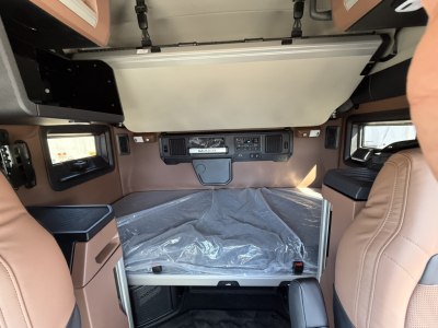 Mack AN64T64 sleeper cab interior with bunk bed platform and overhead storage, front dashboard with controls, brown leather seats, and covered mattress.