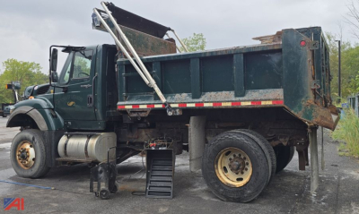 Dump truck side view showing 2010 International WorkStar 7600 with a raised dump body and spare wheel, auxiliary steps, and fuel tanks.