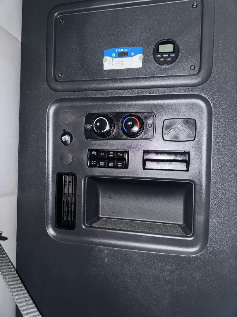 Cab interior panel showing control dials and small display screen, cup holder area, and vent, in Freightliner Cascadia truck