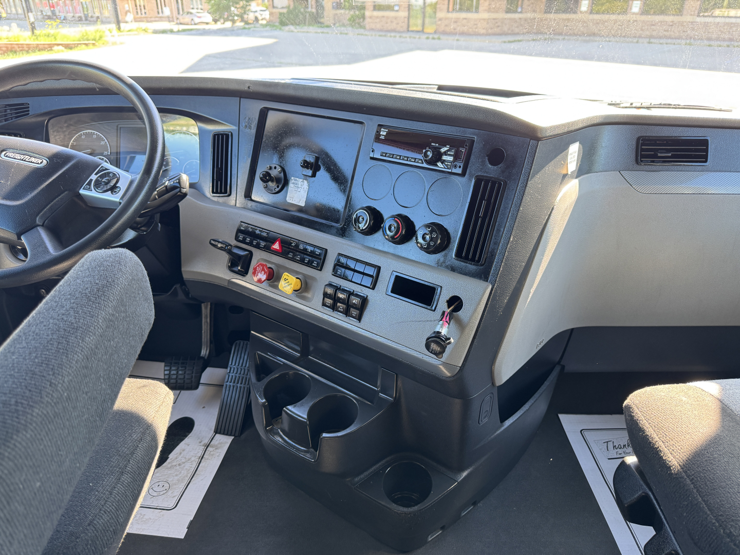 Truck interior dashboard of a Freightliner Cascadia 126 showing steering wheel, instrument cluster, center console with switches, vents, and cup holders.