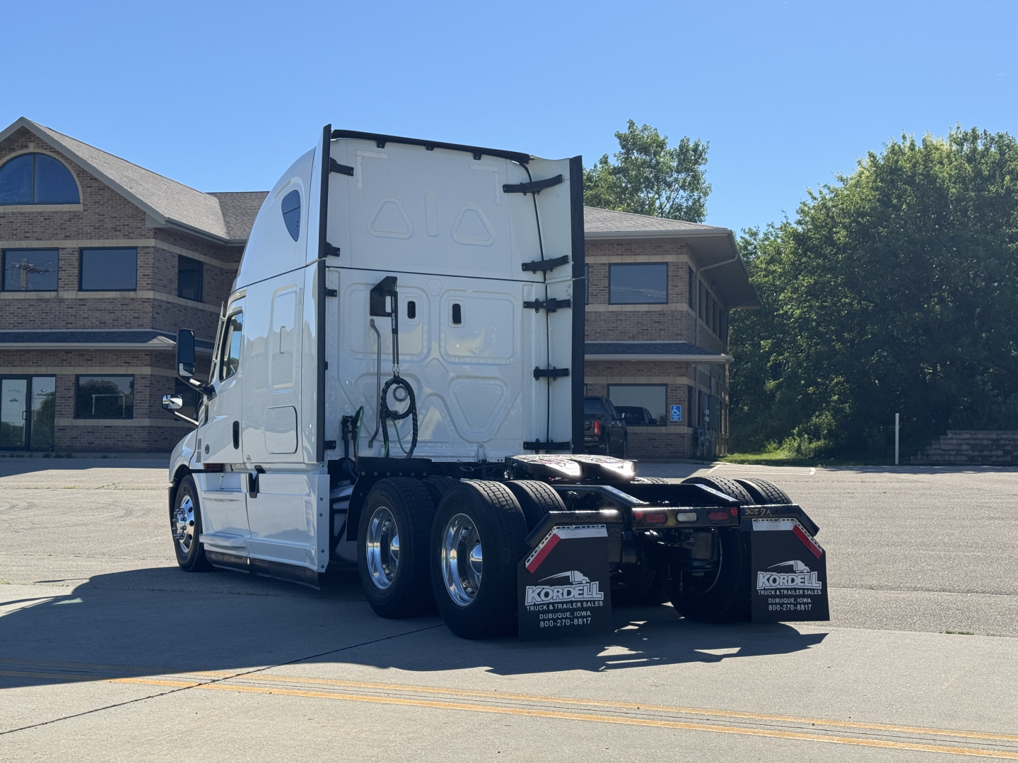 Freightliner Cascadia 126 tractor in a parking lot, rear view showing dual rear axles and sleepers, white paint.