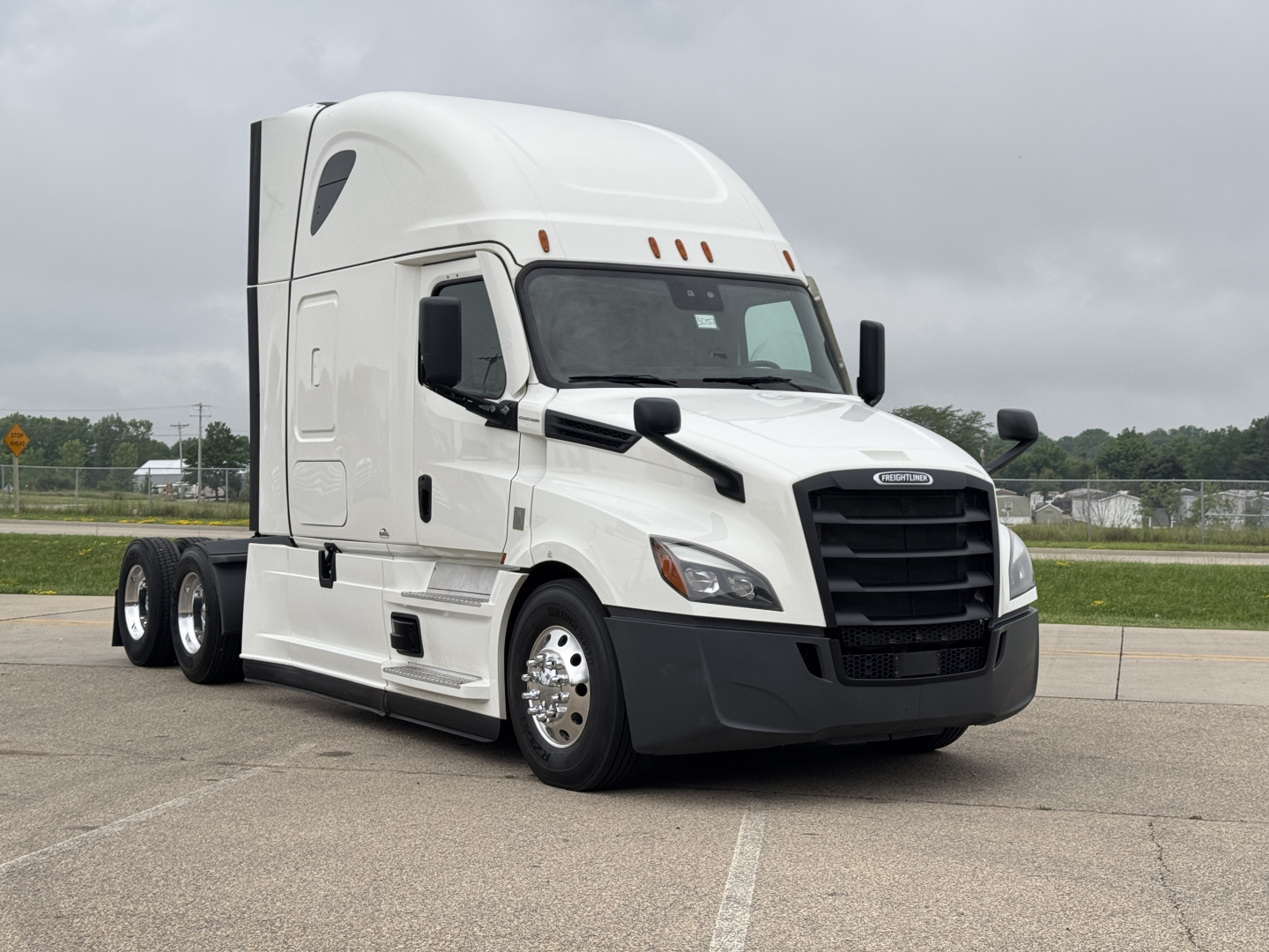 Truck cab with Freightliner badge showing a large black grille, white exterior, and sleeper cab; no visible text other than potential brand emblem on grille