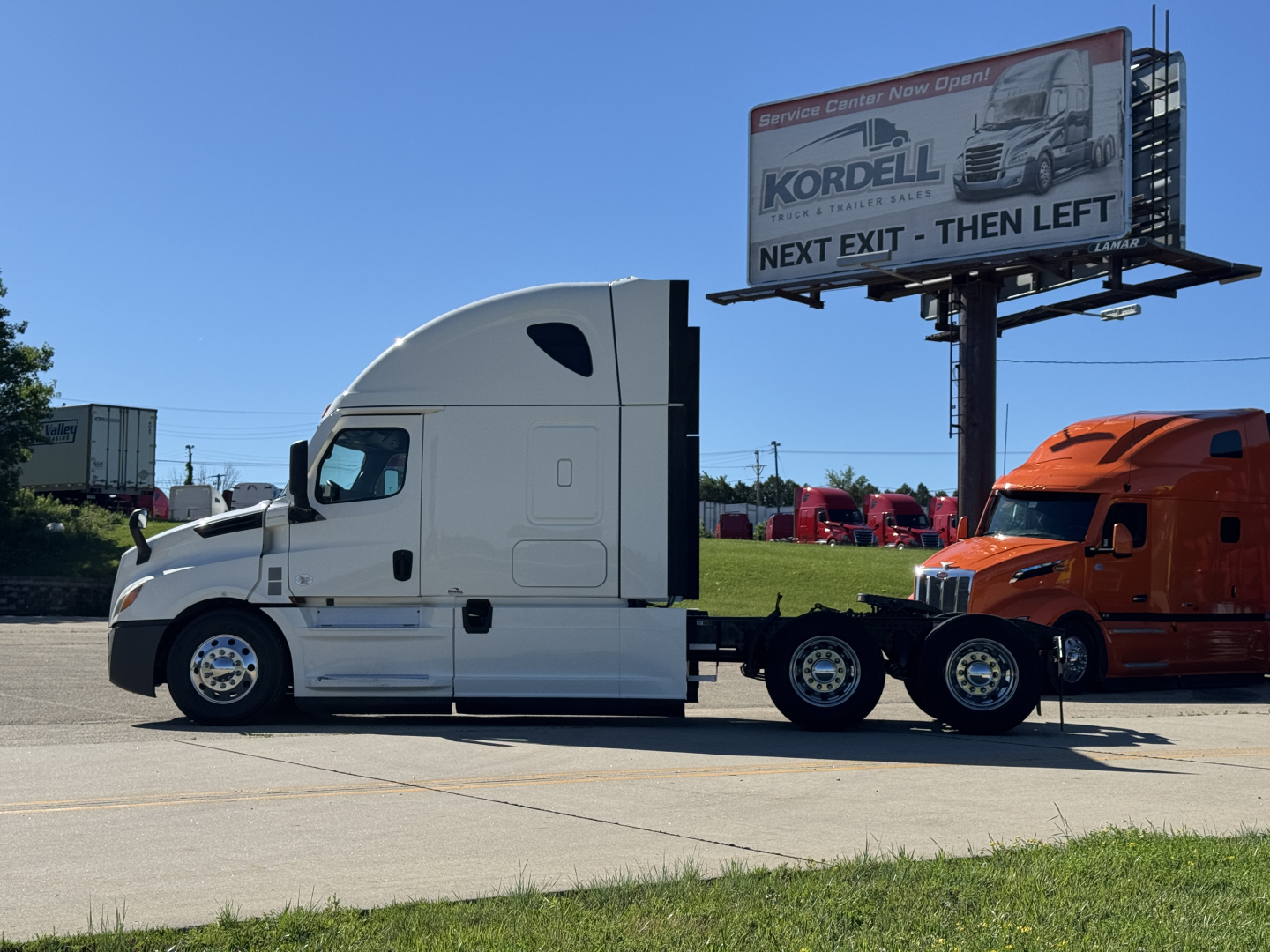 Truck tractor in white with sleeper cab and attached 2-axle trailer on road. Billboard in background reads Kordell and Next Exit Then Left.