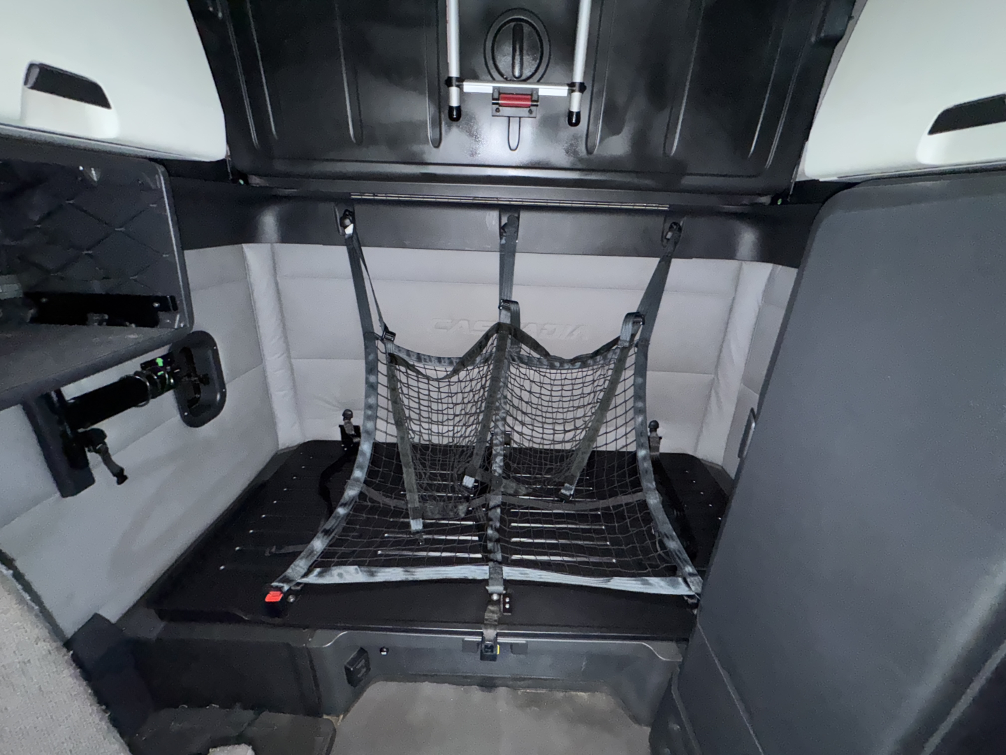 Freightliner Cascadia truck interior showing rear sleeper area with a cargo net over a flat floor; side panels and wall padding visible.