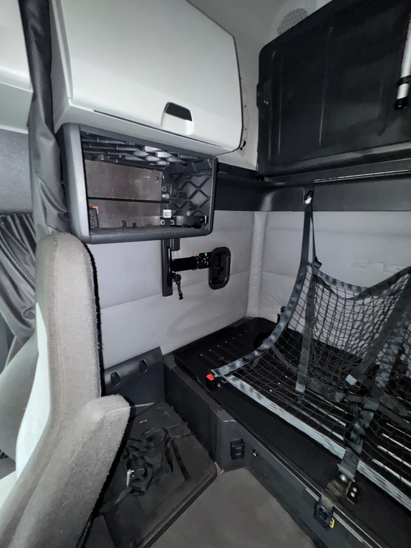 Truck sleeper cab interior with storage compartments, a mesh partition, and a small control panel; no legible labels or fluid markers visible.