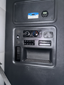 Cab interior panel showing control dials and small display screen, cup holder area, and vent, in Freightliner Cascadia truck