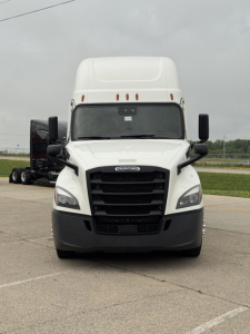 Front view of a white Freightliner Cascadia 126 truck with large black grille, headlights, mirrors, and a high sleeper cab.