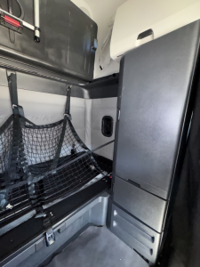 Freightliner Cascadia 126 sleeper cab interior showing storage nets, side cabinet, and vertical grab handle with netting on wall.