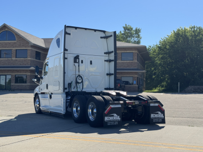 Freightliner Cascadia 126 tractor in a parking lot, rear view showing dual rear axles and sleepers, white paint.