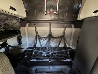 Freightliner Cascadia 126 sleeper cab interior cargo area with netted storage and overhead storage compartments.