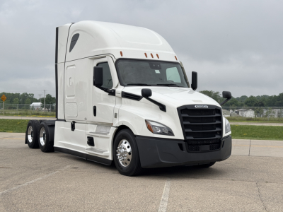 Truck cab with Freightliner badge showing a large black grille, white exterior, and sleeper cab; no visible text other than potential brand emblem on grille