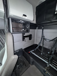 Truck sleeper cab interior with storage compartments, a mesh partition, and a small control panel; no legible labels or fluid markers visible.
