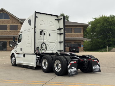 Freightliner Cascadia tractor rear three-quarter view showing dual rear axles, white cab, side windows, and undercarriage components.