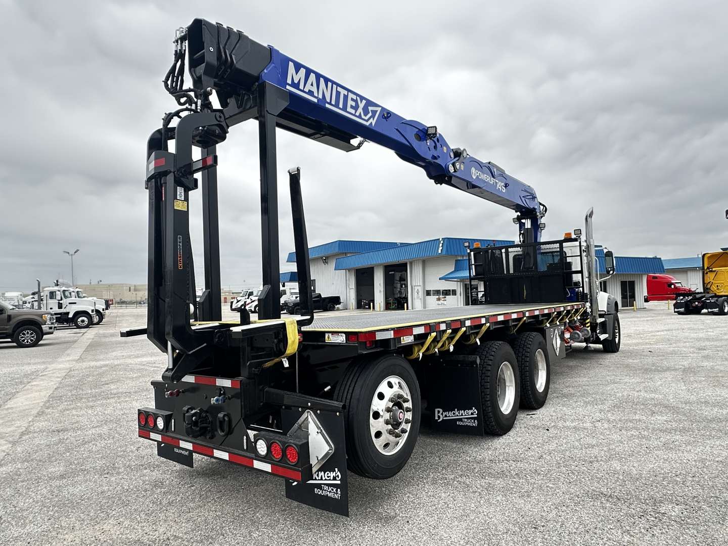 Mack GR64F cab and chassis with a Manitex crane mounted on a multi-axle trailer, side view showing crane arm and rear deck with warning tape.