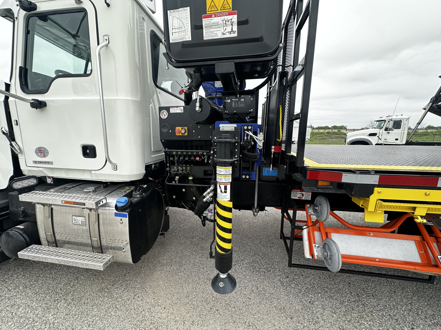 Mack GR64F chassis image showing front cab area with connected control panel and hydraulic landing gear, black and yellow striped stabilizer leg visible.