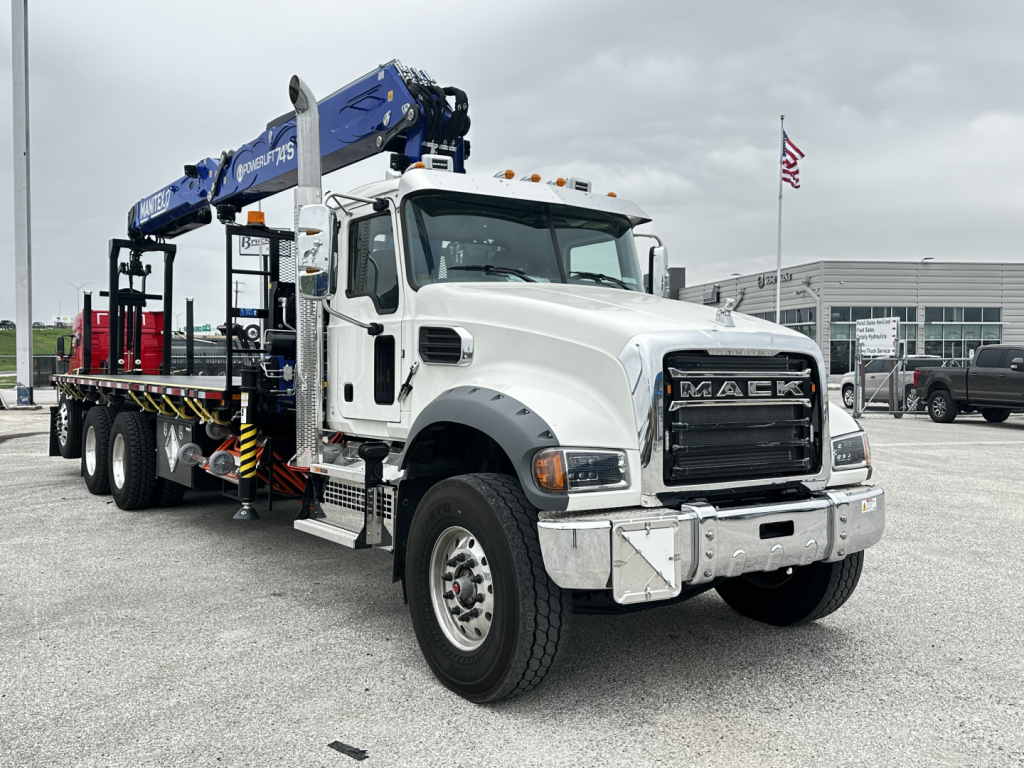 Mack GR64F cab and chassis truck showing front grille with chrome bumper and blue crane booms mounted on flatbed.