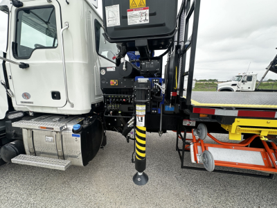 Mack GR64F chassis image showing front cab area with connected control panel and hydraulic landing gear, black and yellow striped stabilizer leg visible.