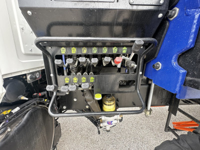 Panel with multiple labeled connectors and levers on Mack GR64F cab chassis, with a yellow hydraulic reservoir and wiring harness visible.