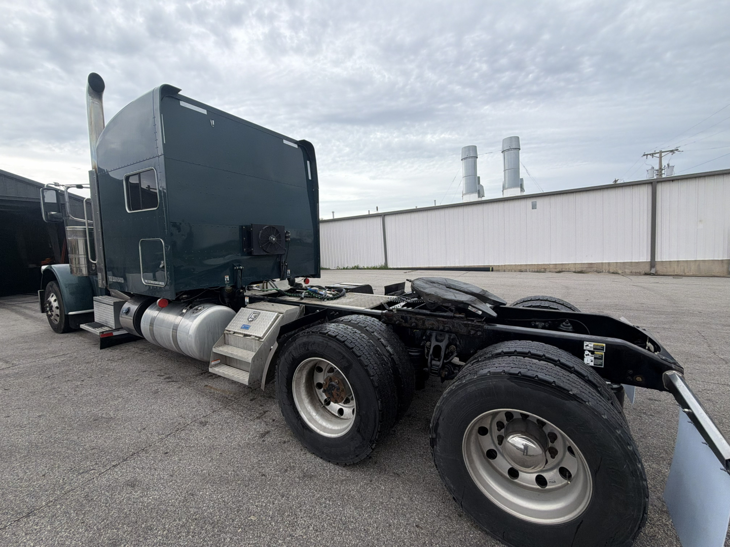 Peterbilt 389 convention sleeper tractor chassis view showing rear axles and fuel tanks with VIN label and stock number in lot.