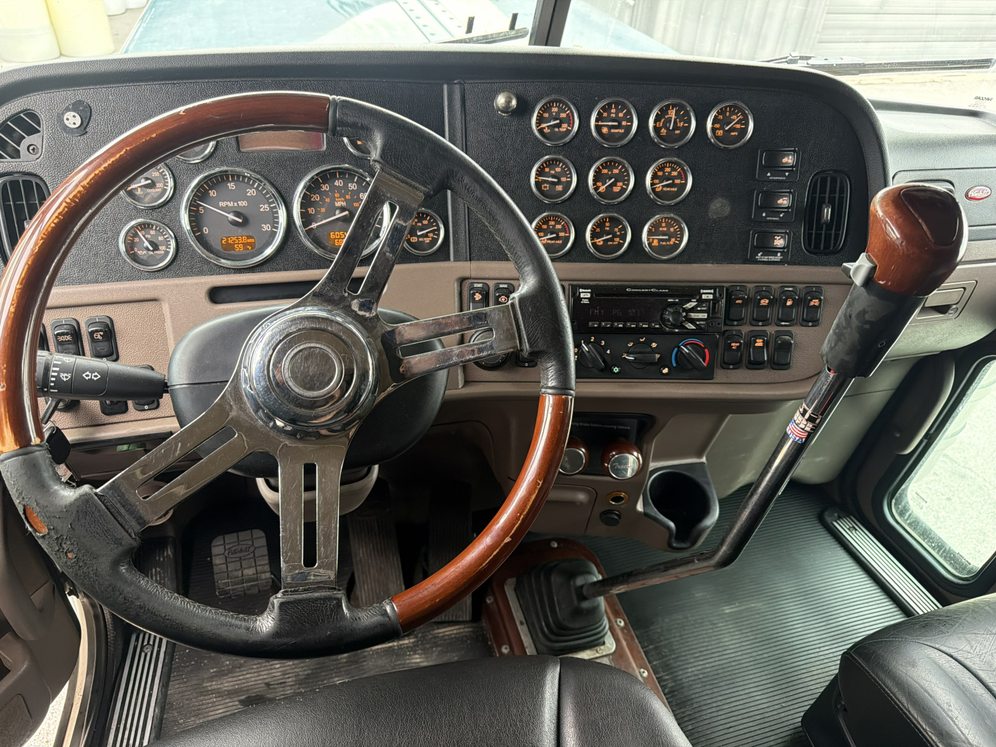 Peterbilt 389 truck dashboard view showing steering wheel, multiple gauges, gear shifter, and control panel.