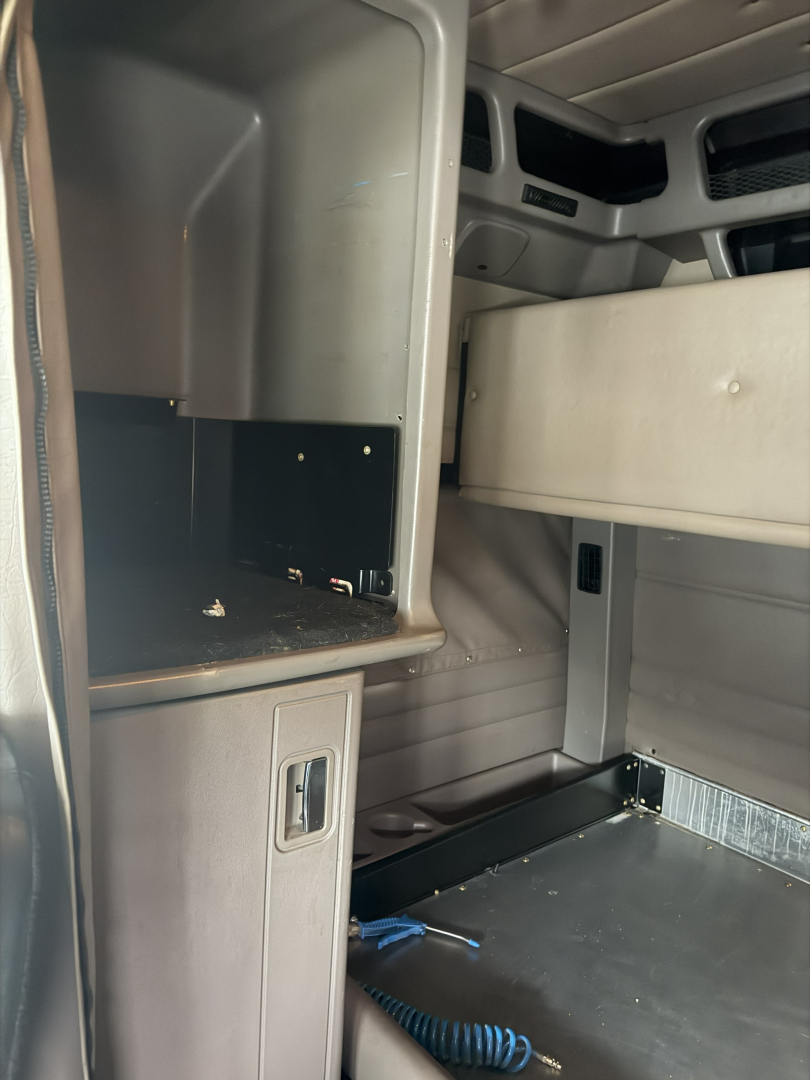 Peterbilt truck cab interior showing upper bunk area and open compartments with shelving and cords inside the sleeper cab.