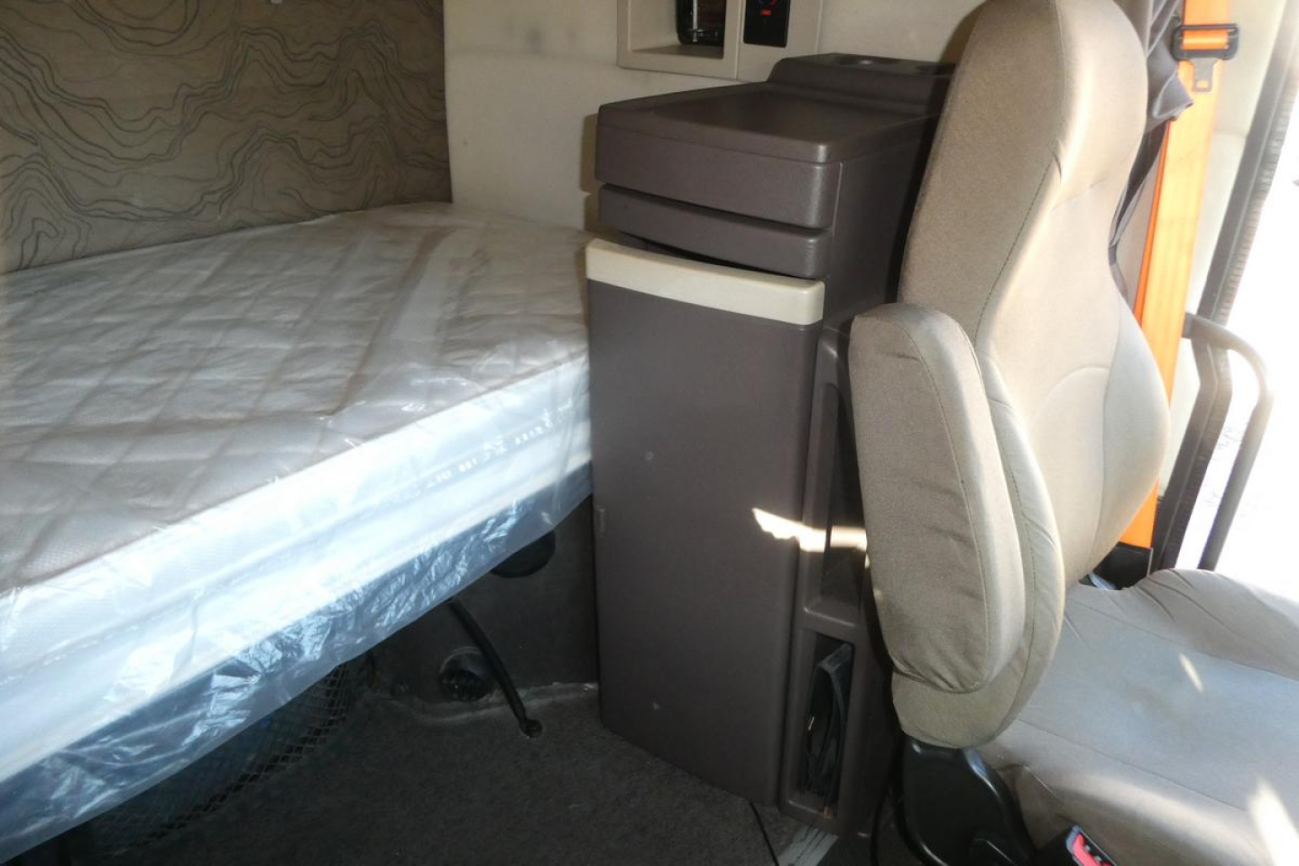 Volvo VNM sleeper cab interior showing bed and driver seat together with storage cabinet.