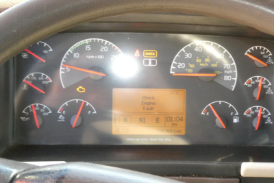 Dashboard cluster of a Volvo truck showing multiple gauges and a central digital display. Visible text includes Check Engine and various gauge readings. No clear part labels beyond generic truck instrumentation.