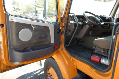 Orange Volvo VNM truck cab interior with open door, steering wheel, dashboard, and speaker panel visible.